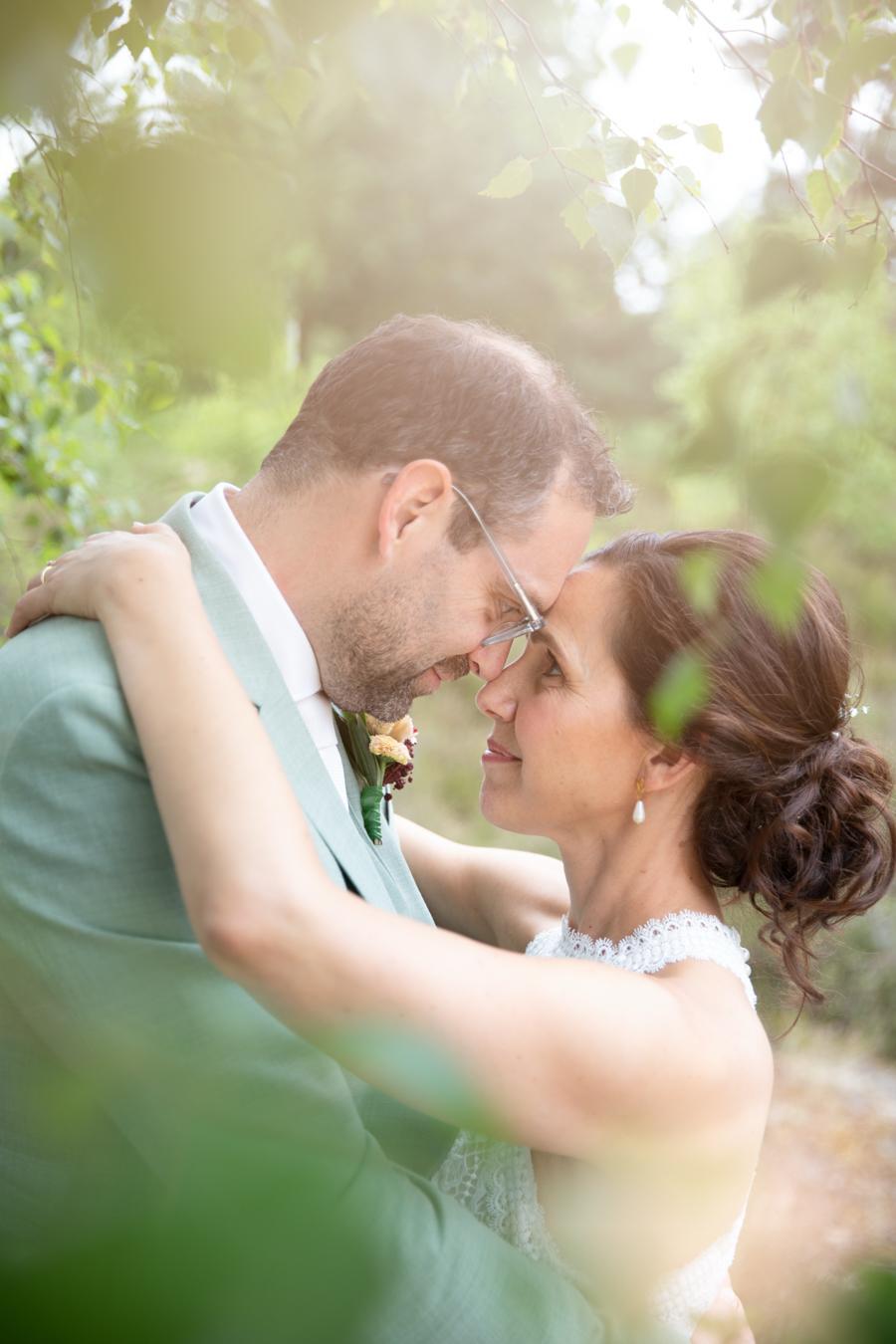 Bride and groom kissing under dappled sunlight through leaves