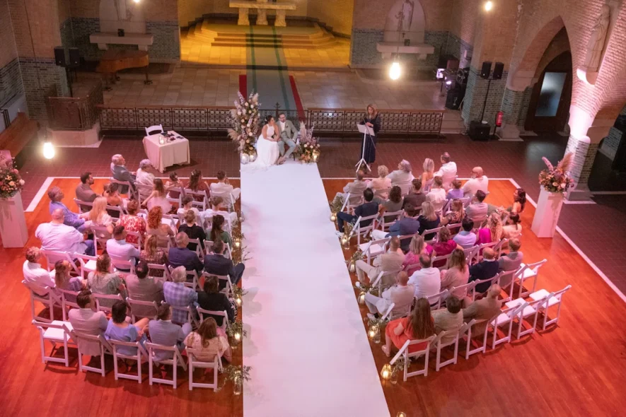 Wedding ceremony in brick chapel with white aisle and pink lighting