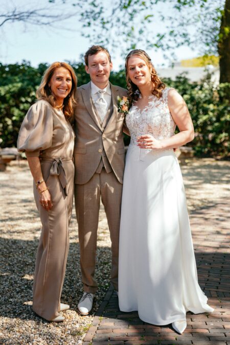 Bride and groom pose with woman in elegant garden setting