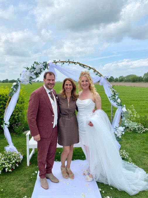 Bride and groom with officiant under floral arch outdoors