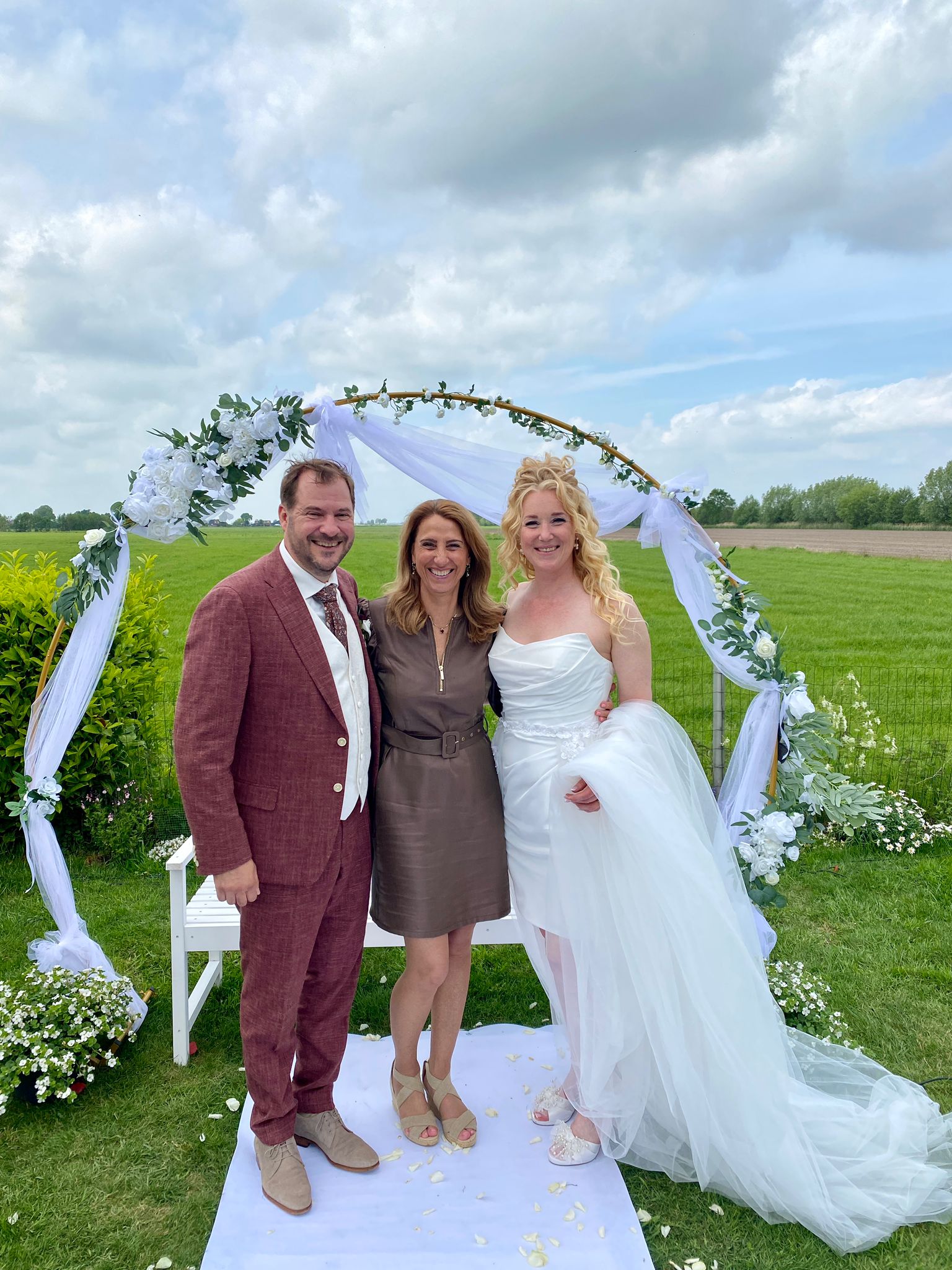 Bride and groom with officiant under floral arch outdoors